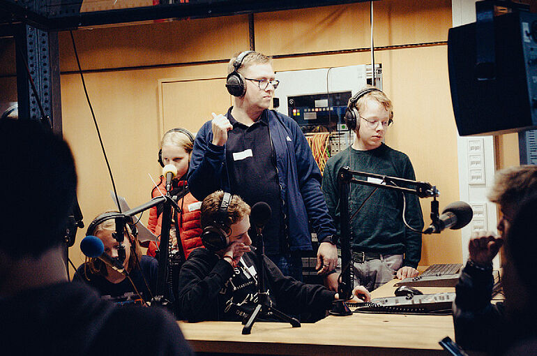 Man sieht einen Mann und Schüler*innen in einem Tonstudio