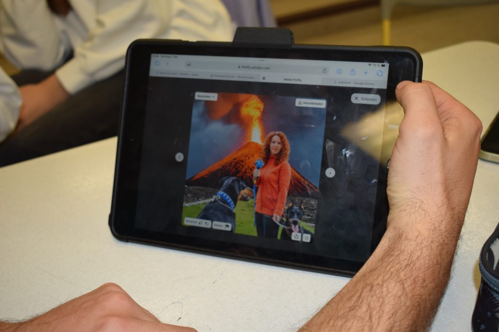 Eine Hand hält ein Tablet auf dem ein KI generiertes Bild zu sehen ist. Auf dem Bild steht eine Frau vor einem ausbrechenden Vulkan, zusammen mit zwei Hunden.
