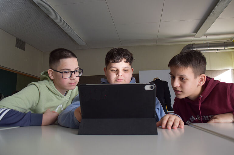 Drei Jungs schauen gemeinsam auf einen Laptop