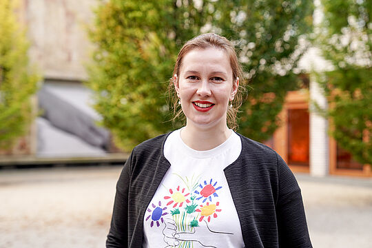 Man sieht eine Frau mit rotem Lippenstift in die Kamera lächeln.